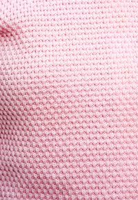 Ανοιχτό ροζ υφασμα με υφή και σχέδιο πλέγματος, με μικρές, ανυψωμένες κουκκίδες σε όλη την επιφάνεια. Μαλακό, πλεκτό υλικό, κατάλληλο για ρούχα ή αξεσουάρ.