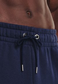 Dunkelblaue Sweatpants mit verstellbarem Bund, ausgestattet mit Metallösen und einer weichen Textur. Sichtbares elastisches Taillendetail.