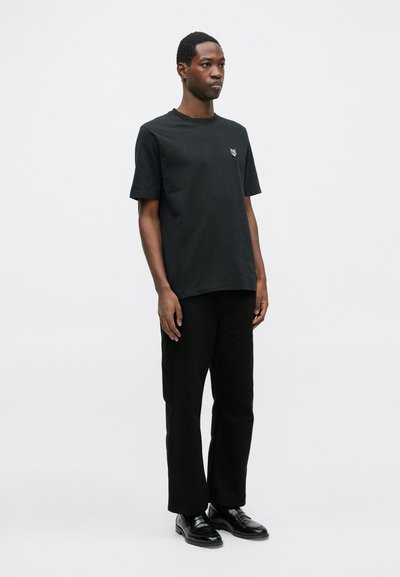 Tricou din bumbac negru cu decolteu rotund și mâneci scurte, având un mic logo brodat pe piept. Asortat cu pantaloni negri și încălțăminte.