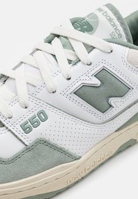 Białe i jasnoróżowe buty sportowe z siateczkowych i zamszowych materiałów, z numerem "550" w jasnoniebieskim kolorze oraz perforowanymi detalami na cholewce.