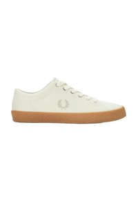 Zapatilla de lona blanca con suela de goma texturizada en color marrón, presenta cinco ojales y un emblema bordado sutil en el lateral.