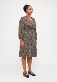 Robe en imprimé léopard en tissu léger, dotée d'un col en V, de manches longues et d'une taille cintrée, associée à des chaussures noires à petits talons.