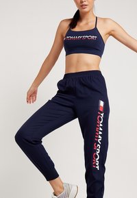 Marineblauw sportief crop top met het "TOMMY SPORT" logo in rood en wit; gecombineerd met bijpassende joggers met zijstrepen en elastische boorden.