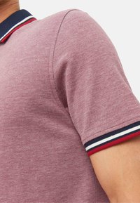Koszulka polo w fakturowanej tkaninie w burgundowym kolorze z granatowym kołnierzykiem oraz czerwono-białymi paskami na rękawach. Krótkie rękawy, dopasowany krój.