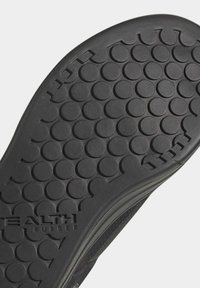 Černá gumová podrážka boty s kruhovým vzorem a vodorovnými drážkami. Obsahuje značení 'Stealth Rubber' poblíž okraje.