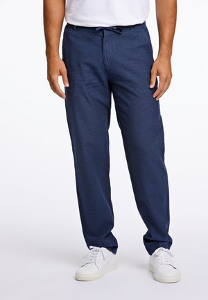 Pantalones de lino azul marino con un corte relajado, que presentan una cintura con cordón y bolsillos, combinados con zapatillas blancas. Textura suave, sin patrones.