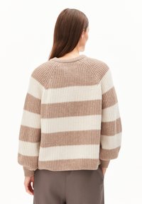 Pull en maille épaisse à rayures beiges et crème. Présente un col arrondi et des coutures d'épaule décalées. Texture douce et coupe décontractée.