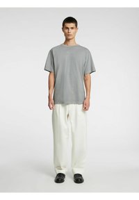 Grå T-skjorte med korte ermer og rund hals, kombinert med løse hvite bukser og svarte sko. Enkel design, glatt stoff, avslappet passform.