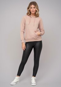 Felpa rosa chiaro con coulisse, tasca kangaroo e polsini a coste, abbinata a leggings neri e sneakers bianche. Texture del tessuto liscia.