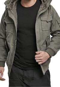 Kurtka typu bomber w oliwkowo-zielonym kolorze z kapturem, z przodu zapinana na zamek, z wieloma kieszeniami oraz ściągaczami na mankietach i dole. Nosi się ją na czarnej koszulce.