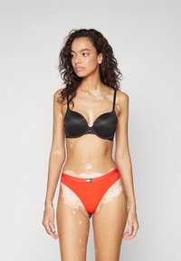 Zwarte gevoerde bh met verstelbare bandjes, gecombineerd met felrode bikini-botten met een logotag. Soepele textuur en aansluitend ontwerp.