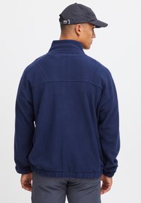 Pullover in pile blu navy con colletto alto, orlo elasticizzato e maniche raglan. Texture morbida con cuciture minime.