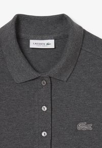 Mörkgrå polo skjorta i texturerad tyg, med klassisk krage, tre knappar och en broderad Lacoste-logga på bröstet.