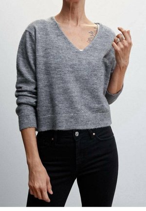 Suéter gris corto con escote en V, puños acanalados y dobladillo. Llevado con jeans negros, que presentan una textura suave y detalles de diseño mínimos.