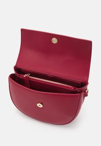 Červená kožená kabelka přes rameno s kulatým tvarem, zlatou kováním a vnitřní kapsou na zip. Interiér je podšitý hladkou tkaninou.