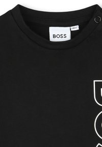 T-shirt nera in cotone con collo rotondo, caratterizzata da un logo e dettagli bianchi. Include un dettaglio a scatto sulla spalla per una maggiore facilità di indossamento.