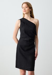 Abito nero a spalla unica con scollo drappeggiato, silhouette aderente e texture sottile, realizzato in un tessuto leggero.