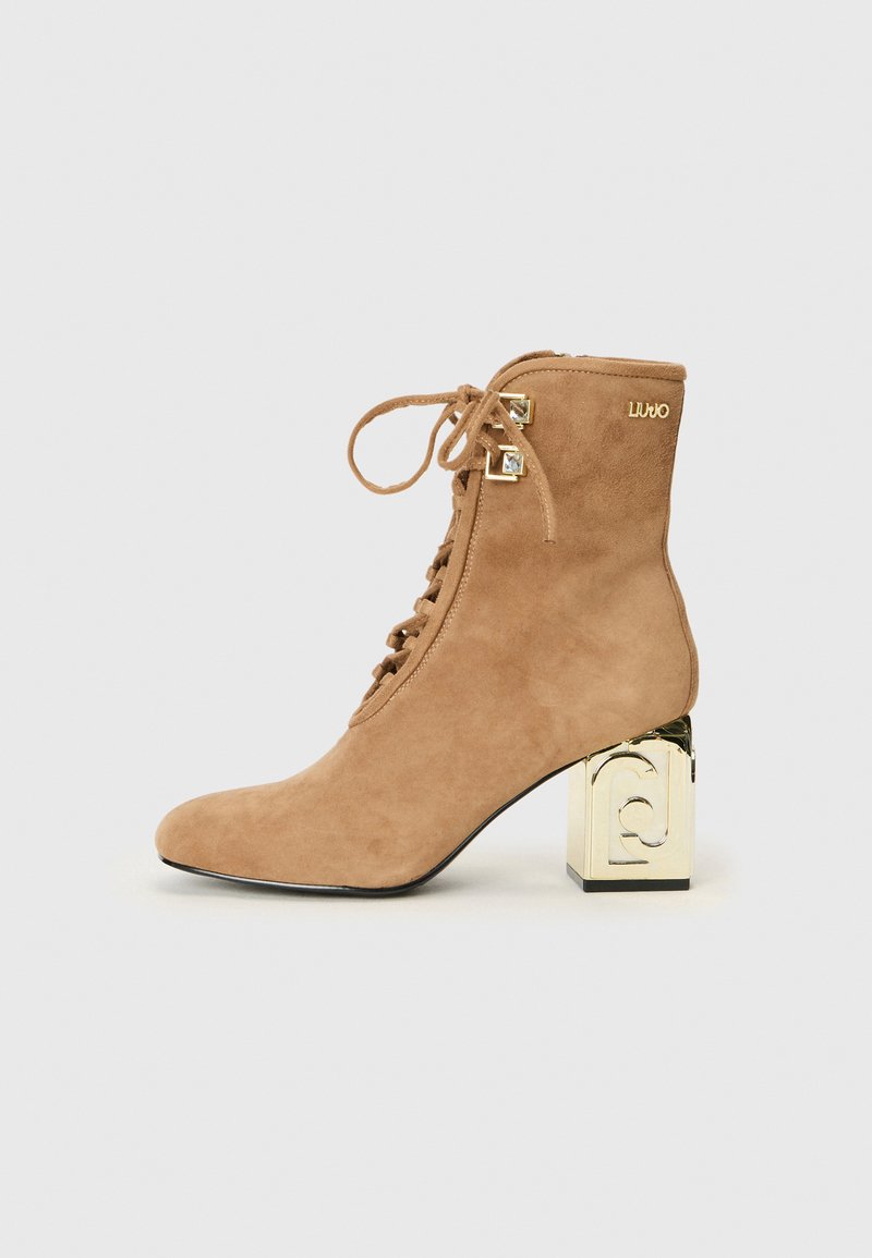 Braune Wildleder-Ankle-Boots mit Schnürung an der Vorderseite, ausgestattet mit einem quadratischen, goldenen Akzentabsatz und einem kleinen goldenen Logo-Detail an der Seite.