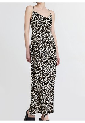 Vrouw draagt een mouwloze, luipaardprint, enkellange slipjurk met dunne bandjes en zwarte hoge hakken.