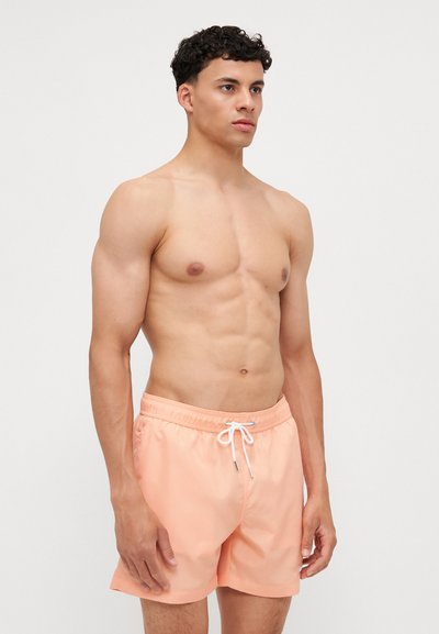 Ferskenen badshorts laget av lett stoff, med elastisk midjebånd og snøring samt en glatt tekstur. Ingen mønstre eller detaljer.