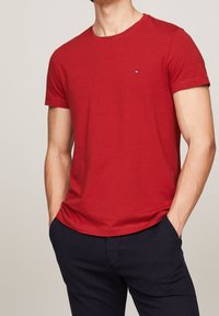 Rød bomulds t-shirt med rund hals og korte ærmer, der har en lille logo detalje på brystet. Sammen med marineblå bukser.