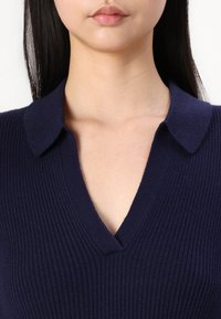 Navy ribbed sweater with a V-neckline and a flat collar, showcasing a soft texture and fitted design.