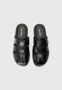Black leather slide sandals featuring woven straps, open toe design, and a cushioned insole. Logo present on the inner sole.