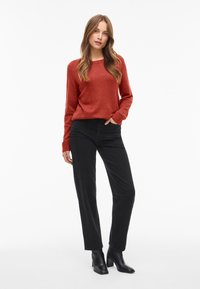 Rustfarget strikkegenser med ribbede mansjetter, kombinert med høyt midjebelte, svarte rette bukser og svarte ankelstøvler.