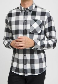 Zwart-witte geblokte button-up blouse met een kraag en een enkele borstzak. Gemaakt van een stof met een zachte textuur en lange mouwen.