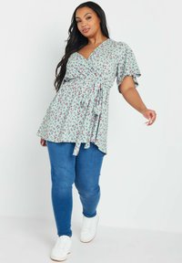 Top avvolgente di un azzurro chiaro con motivo floreale, maniche a sbuffo corte e vita con coulisse. Abbinato a jeans skinny blu e sneakers bianche.