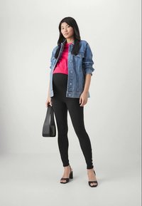 Dongerijakke, rosa topp, svarte leggings med knappedetaljer, svarte høye sandaler og en svart håndveske. Enkelt, figursydd og moderne design.