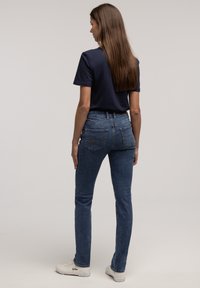 Granatowy bawełniany t-shirt o dopasowanym kroju. Jasnoniebieskie dżinsy z wysokim stanem i lekkim stretchu. Białe sneakersy z czarnym logo.