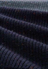 Dunkelblaues strukturiertes Gewebe mit geripptem Muster, das farbenfrohe Sprenkel von Rot und Gelb enthält. Weiches, wollähnliches Material.