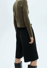 Pull court vert olive et short noir taille haute. Le pull a une texture douce, et le short présente une coupe décontractée avec des poches.