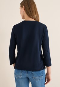 Haut bleu marine à manches longues avec un col rond et une texture lisse. Associé à un jean bleu clair avec des poches arrière et des coutures discrètes.