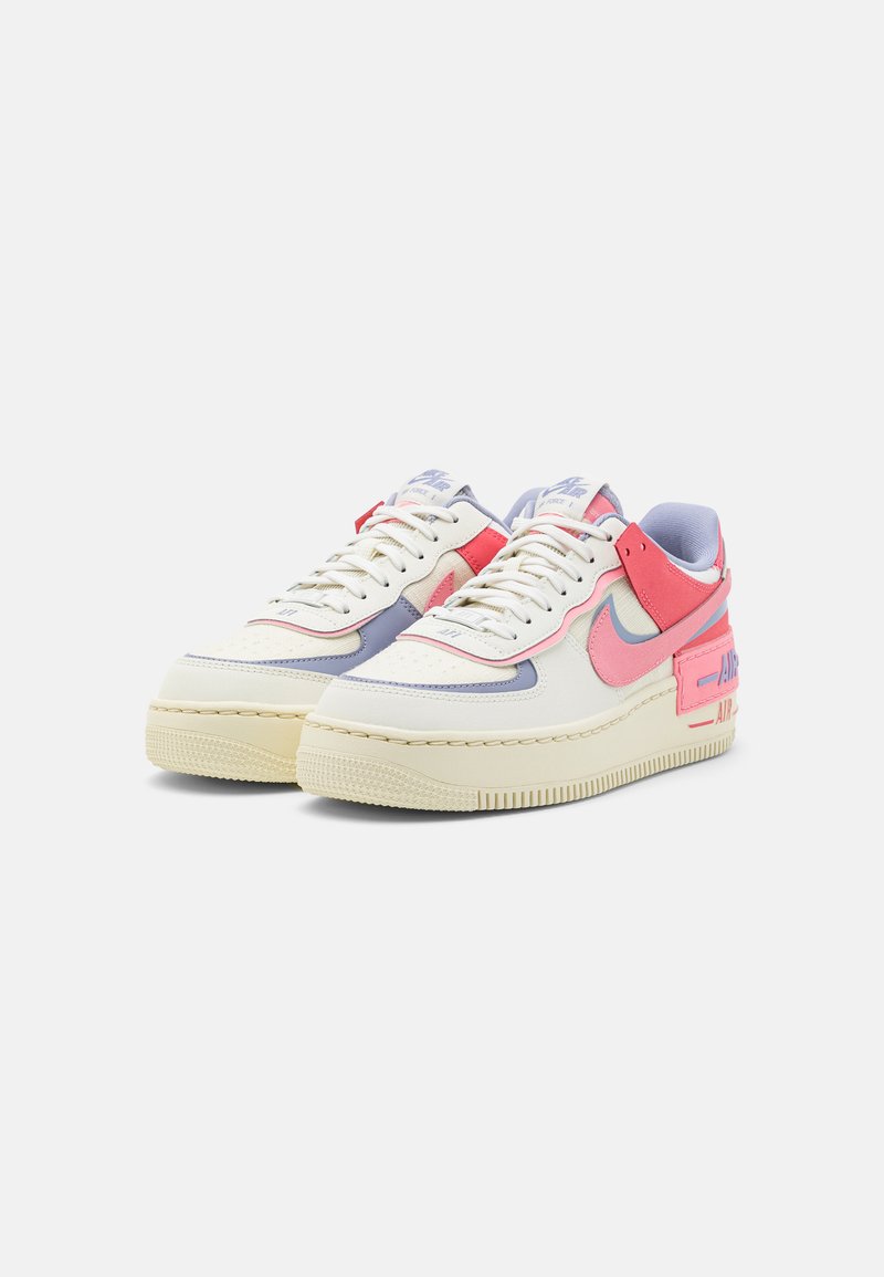 Sneakers Nike Air Force 1 mają cholewkę z kremowej skóry, różowe i jasnoniebieskie akcenty, wyściełany kołnierz oraz teksturowaną gumową podeszwę.