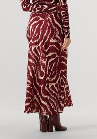 Bordeauxfarbener Rock mit cremefarbenem abstraktem Muster, fließendes Design, weicher Stoff, knöchellang, kombiniert mit braunen Stiefeletten auf einem schlichten Hintergrund.