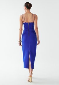 Karališkai mėlyna, prigludusi suknelė su raukšlėtu tekstūra, reguliuojamomis plonomis petnešėlėmis ir užtrauktuku nugaroje. Su aukštai iki šlaunies siekiančiu kirpimu papildomam detalumui.