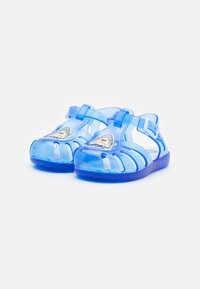 Sandalias de gel transparente azules con correa, diseño abierto y gráfico de tiburón en la parte frontal. Cuenta con una suela texturizada y detalles recortados.