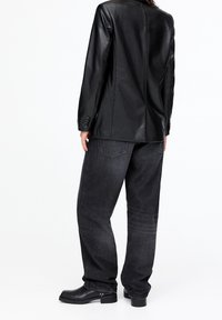 Blazer en cuir noir, coupe ajustée, couture unique au dos. Porté sur un jean taille haute gris foncé à coupe décontractée. Bottines noires brillantes.