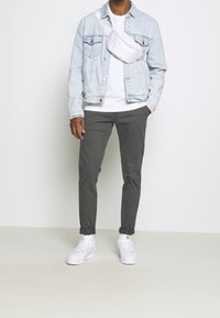 Svetle modrá džínová bunda přes bílé tričko, kombinována se šedými slim-fit kalhotami a bílými sportovními botami. Obsahuje bílou kabelku přes rameno.