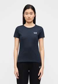 Marineblauw T-shirt met korte mouwen van katoen, voorzien van een ronde halslijn en een klein wit EA7-logo op de borst. Soepele textuur.