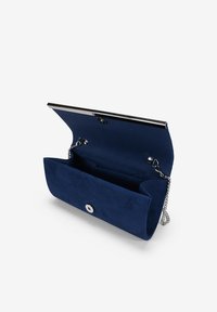 Clutch de ante azul marino con cadena plateada, cierre de metal y un interior con bolsillos. Presenta una textura suave y una forma estructurada.