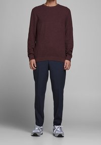 Bordowy sweter z dzianiny z okrągłym dekoltem w połączeniu z ciemnoniebieskimi spodniami. Szare sportowe buty uzupełniają strój.