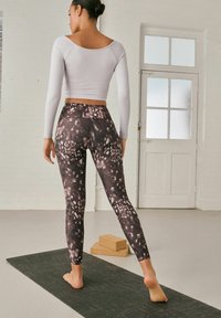 Top corto grigio chiaro, leggings a lunghezza totale con un motivo astratto in nero, bianco e malva, indossati su un tappetino da yoga in un ambiente luminoso.