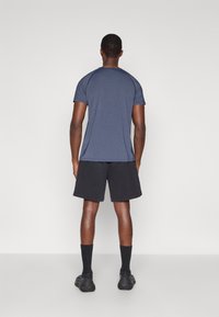 T-shirt atlético azul-marinho de mangas curtas, combinado com calções pretos. O tecido parece suave e leve, adequado para vestuário desportivo.