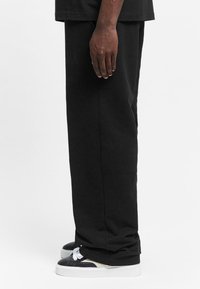 Black, straight-fit sweatpants made of cotton, featuring a smooth texture, with a slight taper towards the ankle, paired with black and white sneakers.
