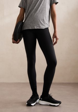 Black leggings with a fitted design, paired with a gray short-sleeve shirt. The person holds a black weight plate in their right hand.