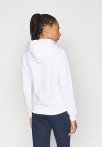 Λευκό φλις φούτερ με κουκούλα, με ριμπ μανσέτες και τελείωμα, φορεμένο με σκούρο μπλε παντελόνι, φαίνεται από πίσω.