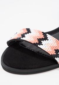 Beaded slide sandal featuring a textured, multicolored strap with pink, black, and white patterns; soft black suede footbed and sole.